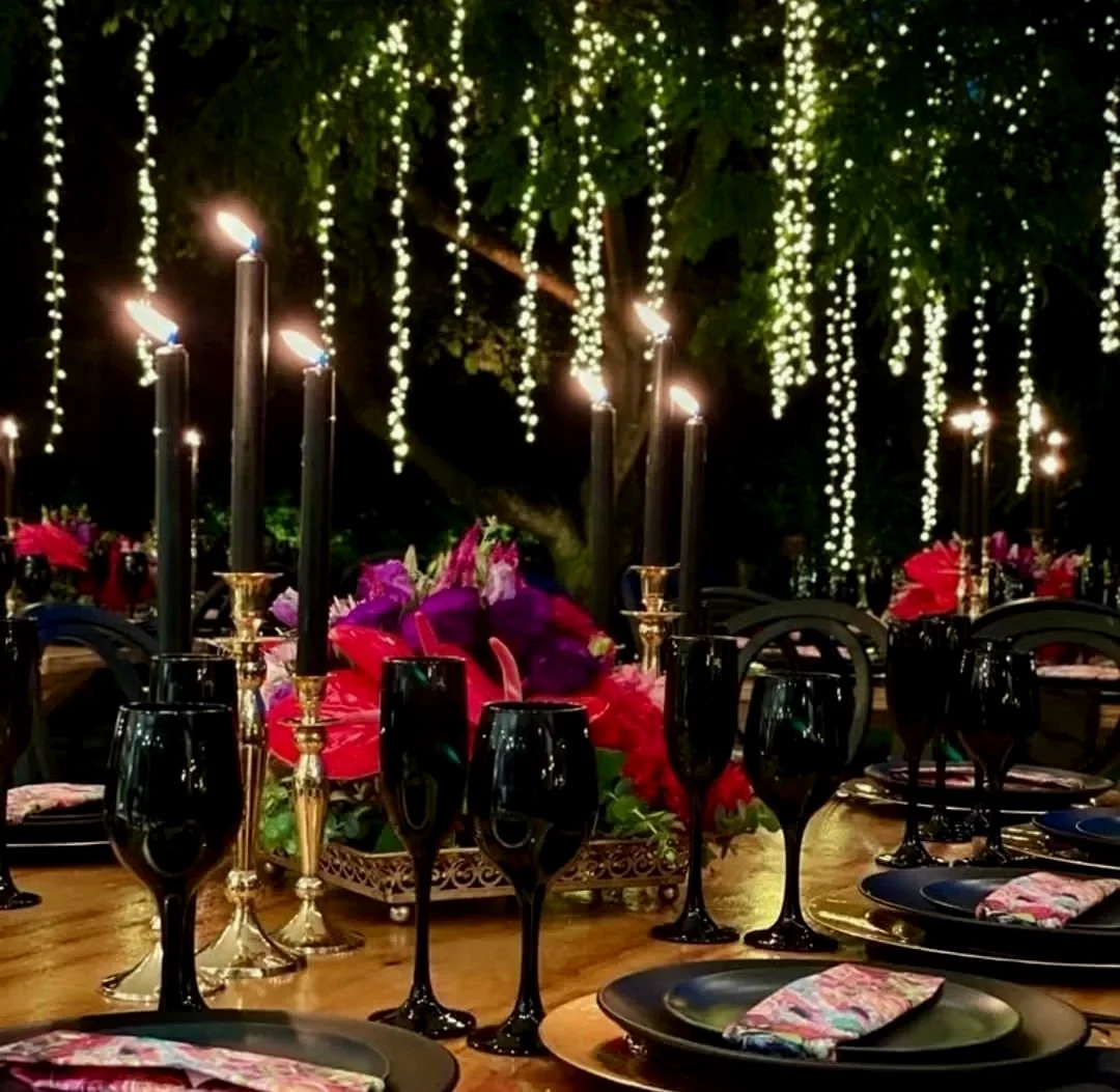 Black taper candles and pink florals on a table, cascading fairy lights behind