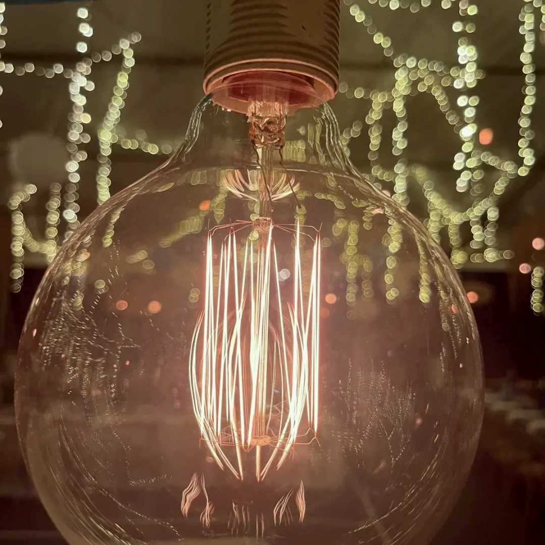A large filament globe photographed close up, glowing warm, with the rest of the rig out of focus behind it