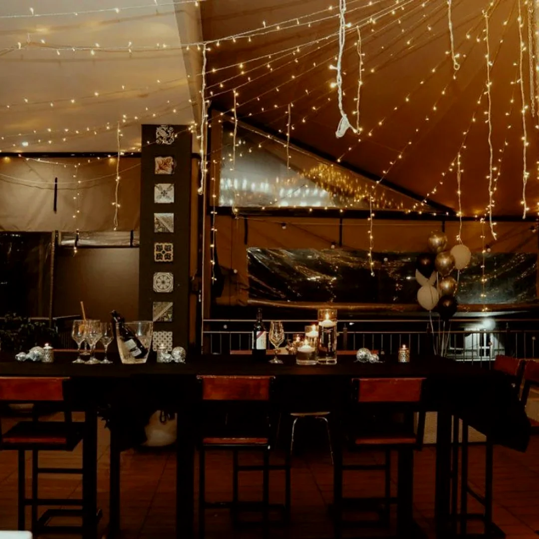 A venue interior with a curtain of fairy light down one wall, festoon strings across the ceiling and tables laid below