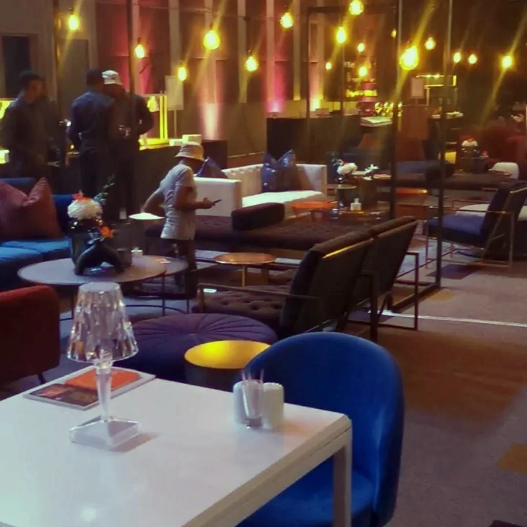 A lounge-style function area lit in deep blue and magenta, with festoon strings overhead and low seating around white tables