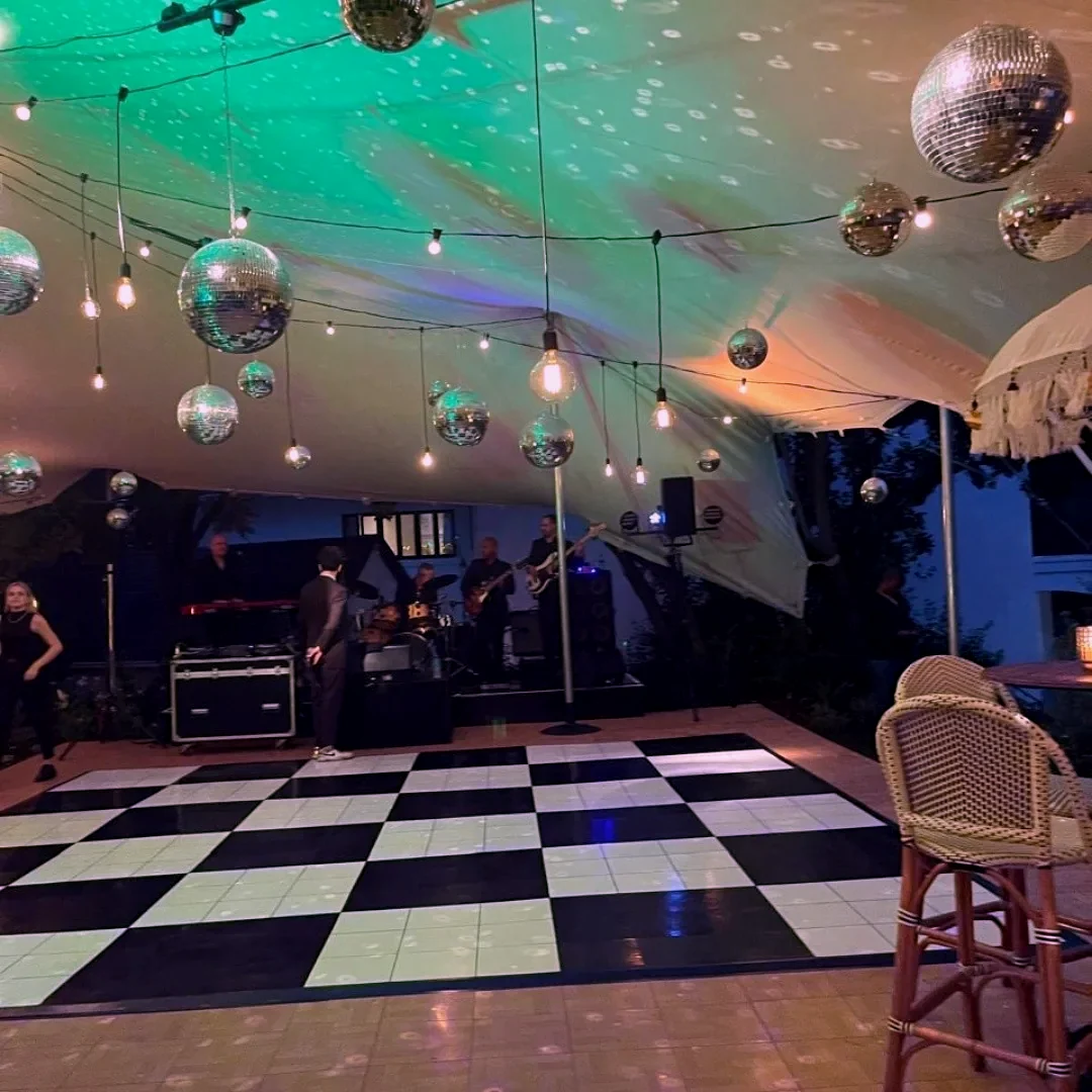 A black and white chequerboard dance floor lit by mirror balls and coloured wash light, with band equipment on a stage behind