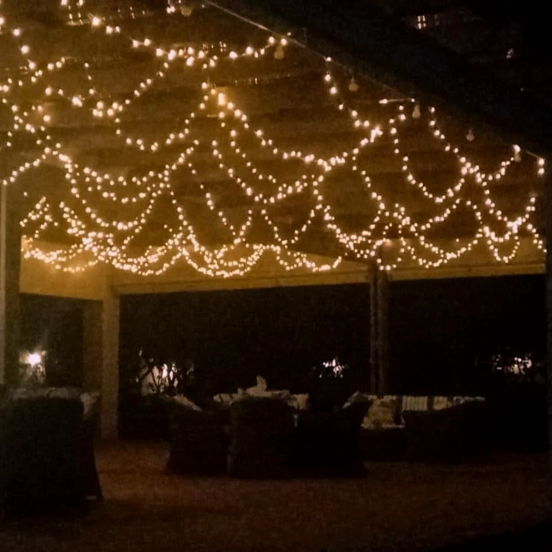 A marquee interior with lines of warm fairy light swagged across the dark roof above a seating area