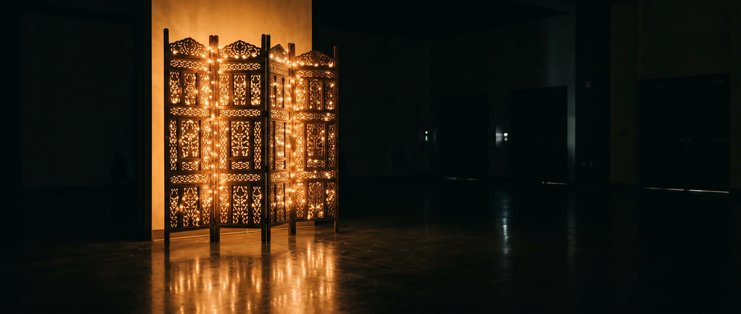 A tall openwork screen threaded with warm light, standing in an empty room before an event