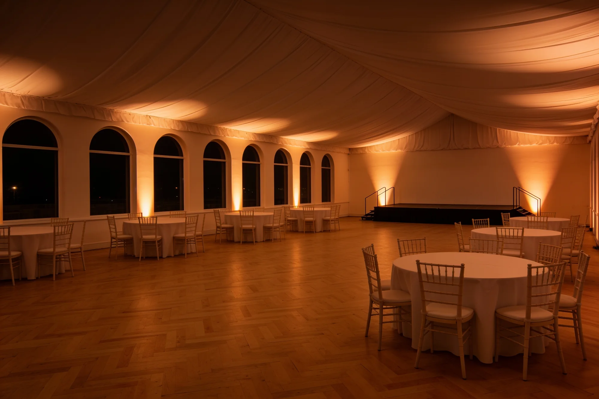 The same hall with warm amber uplighters washing the walls and drapes