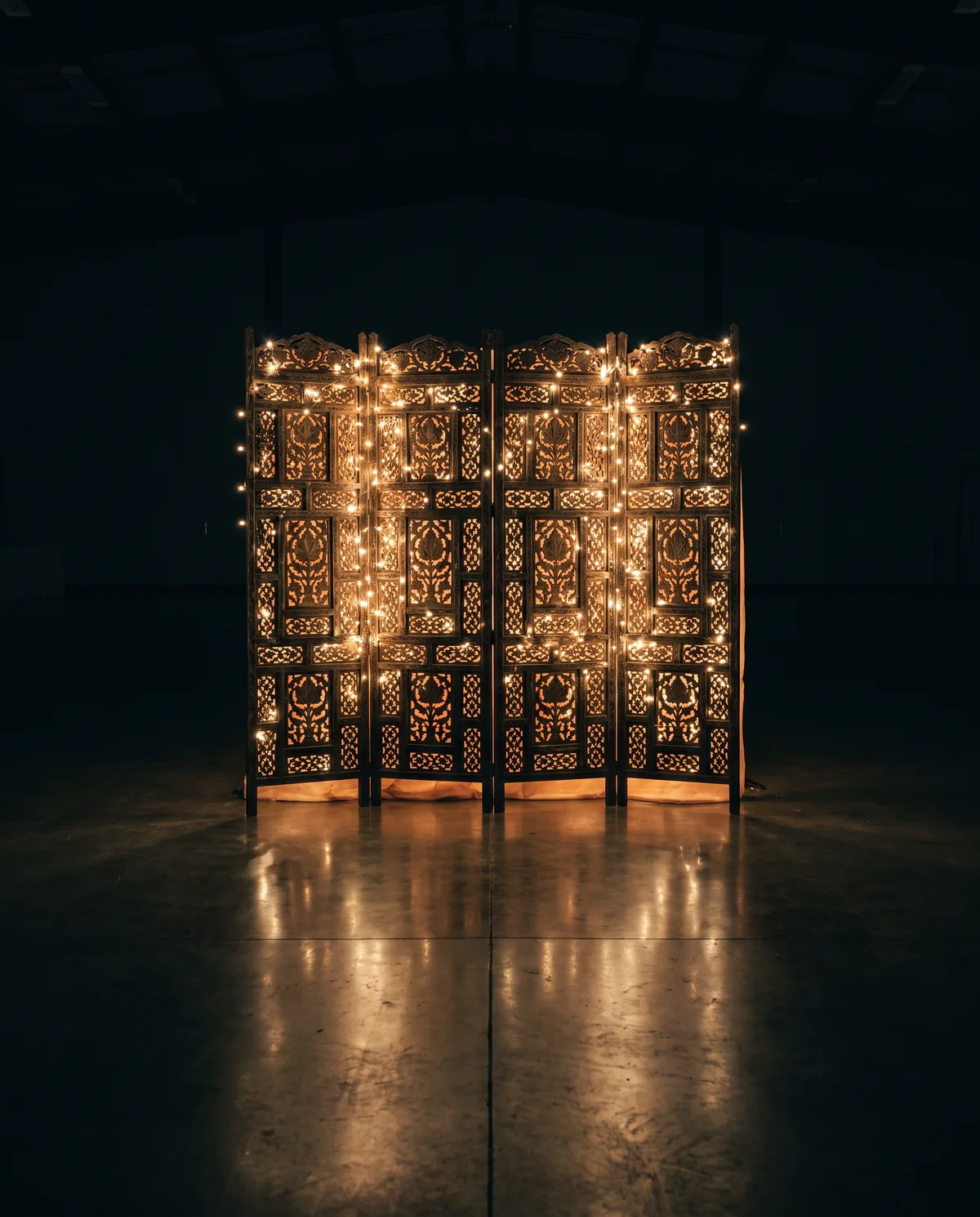 A tall openwork partition screen threaded with warm fairy lights and backlit